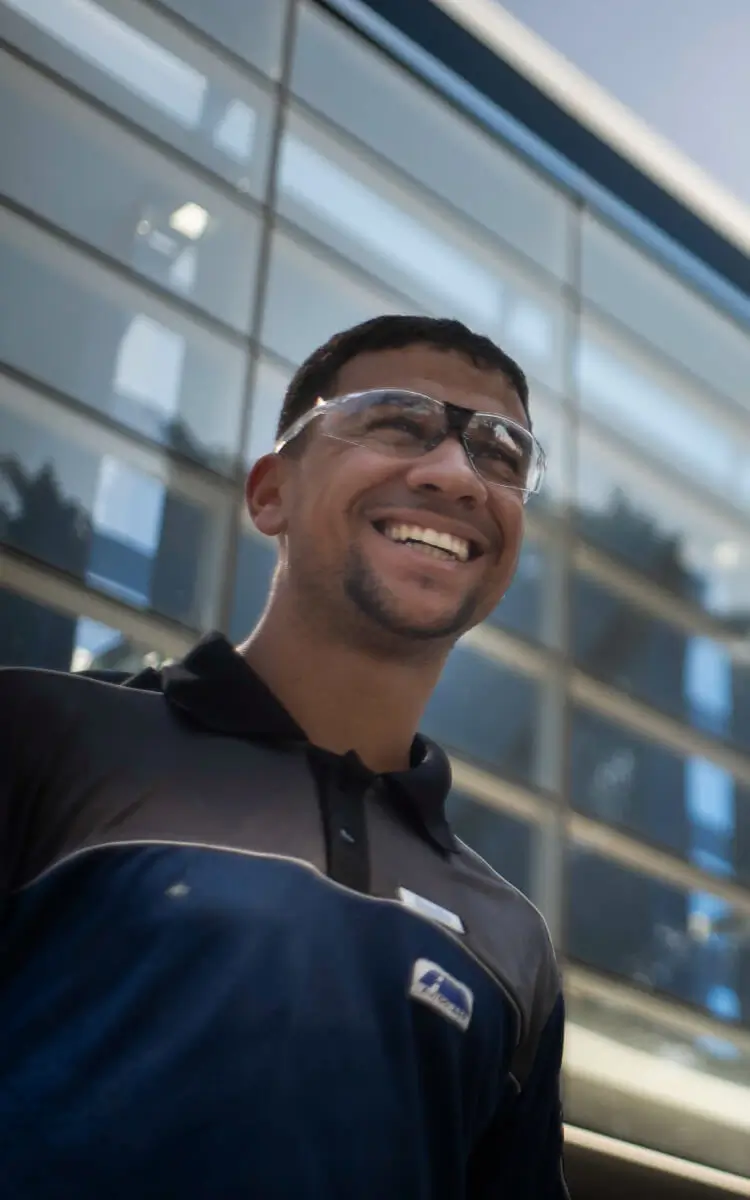 Duas pessoas sorrindo na frente de uma loja de aluguel de carros, em um ambiente moderno com fachada de vidro, promovendo serviço de aluguel de veículos.