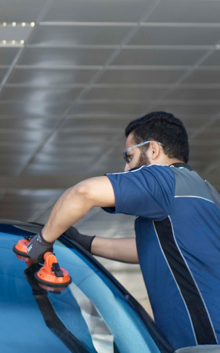 Dois lojistas da empresa Autoglass usando ventosa removendo um parabrisa de um veículo